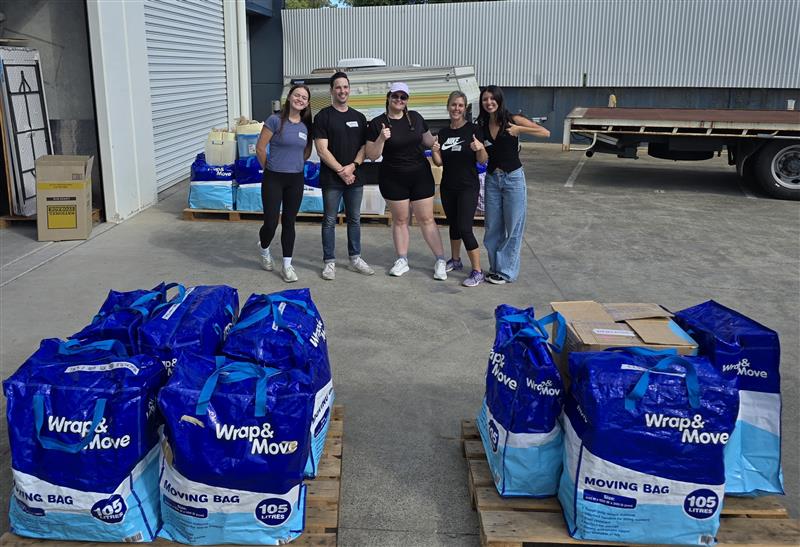 4 people standing with stacks of filled moving bags
